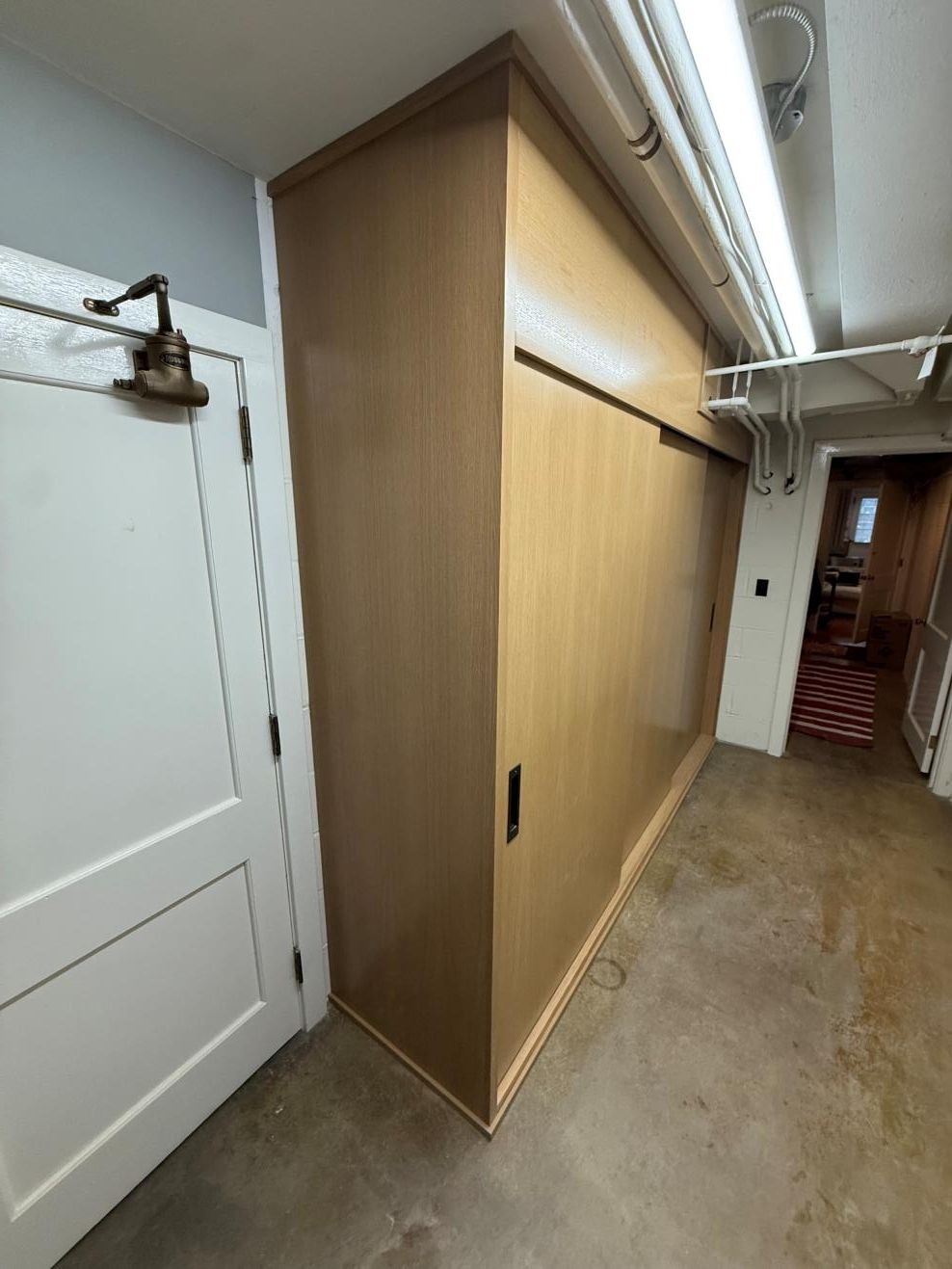 Narrow hallway with a large wooden sliding door beside a white door and exposed ceiling pipes.