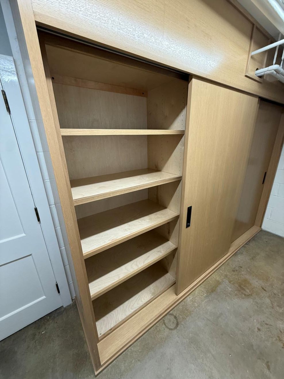 Open closet with built-in wooden shelves and a sliding door in a hallway