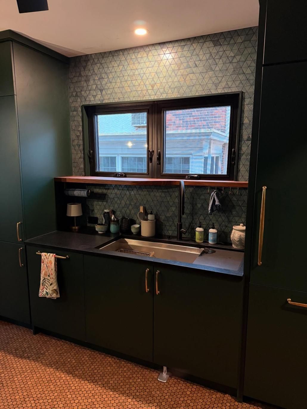 Modern kitchen wet bar with black cabinets, sink, and patterned backsplash beneath a window