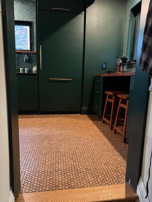 Small dark-green room with tiled floor, cabinet, stools, and a window on the left.