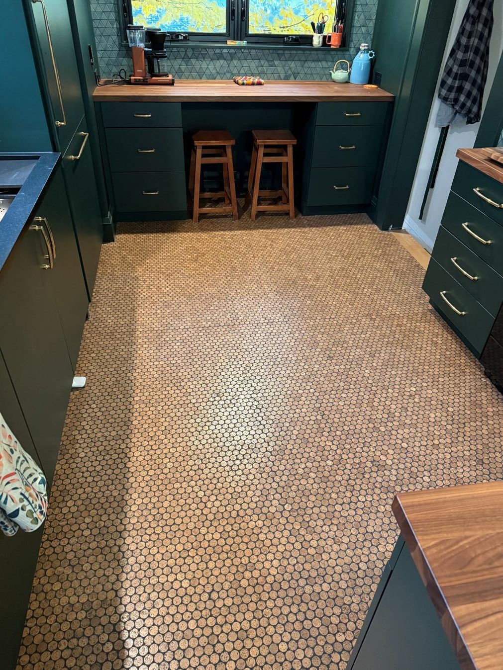 Narrow room with green cabinets, woven rug floor, and a desk by a window with two stools underneath