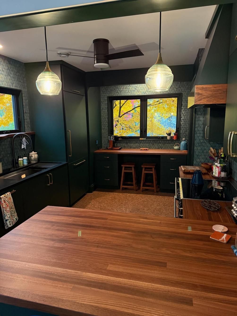 Cozy dark kitchen with wood island, hanging lights, stools, and colorful window art