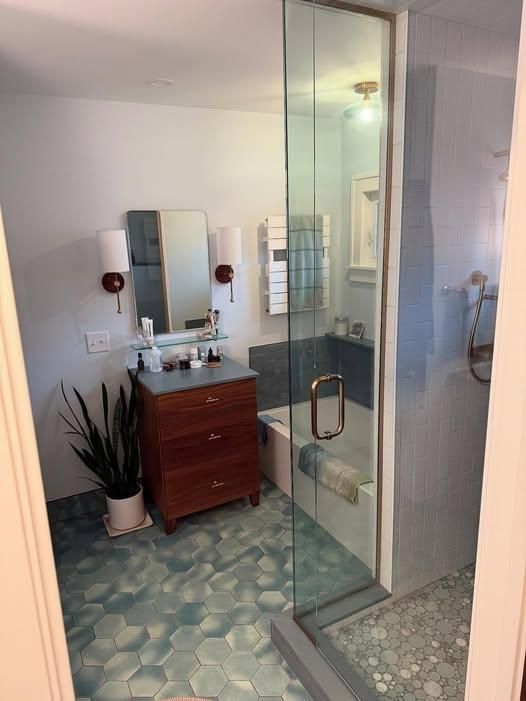 Bathroom with glass shower, patterned tile floor, and wooden vanity with mirror and toiletries
