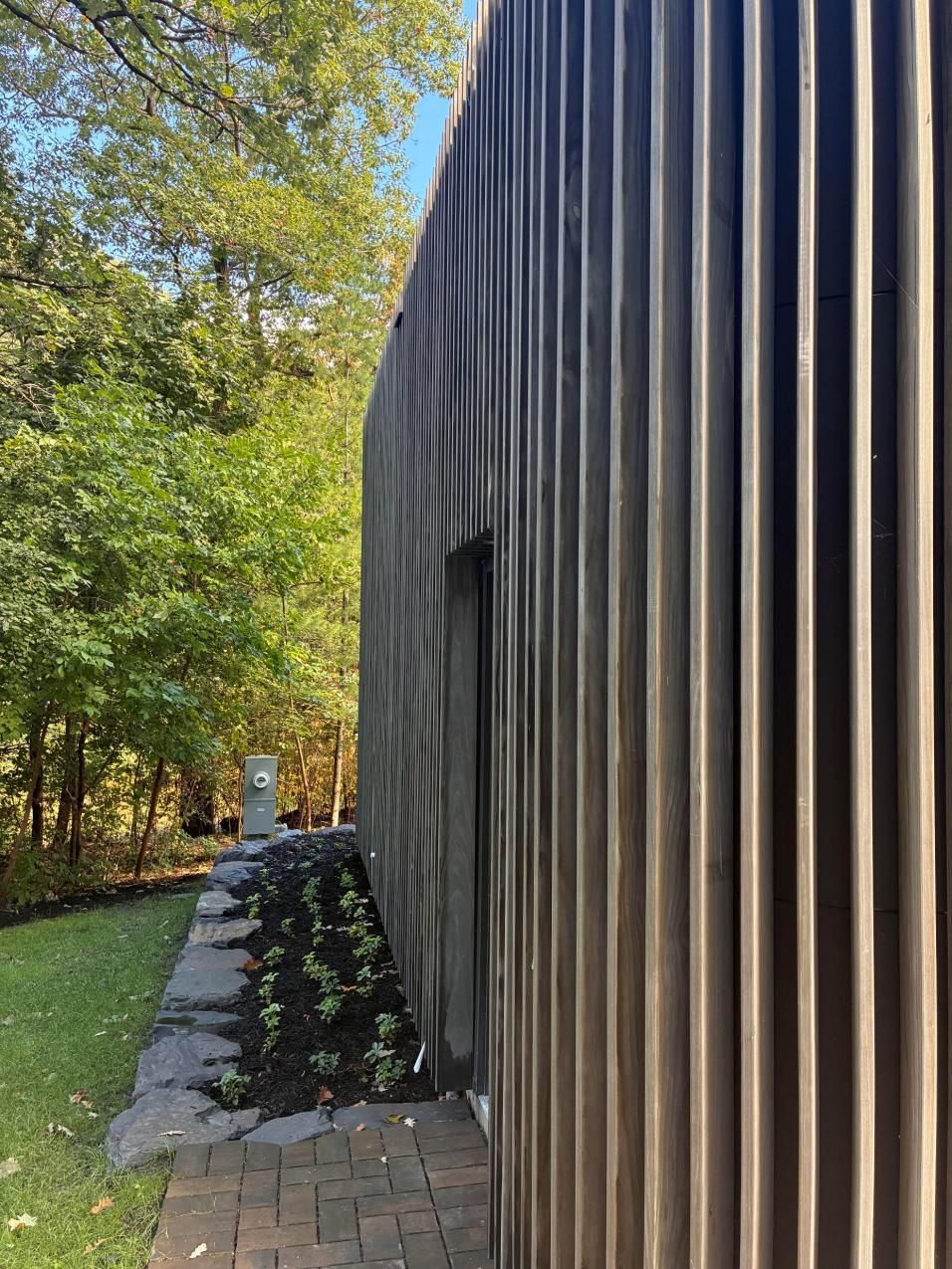 Wooden-sided building beside a leafy garden path with stone edging and trees in autumn light