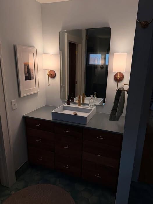 Small bathroom vanity with dark wood cabinets, gray countertop, vessel sink, mirror, and wall sconces.