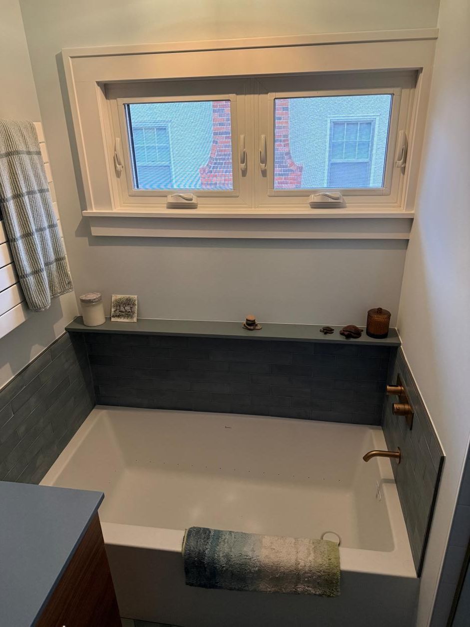 Small bathroom with a white bathtub, blue-gray tile, and a window above the tub.