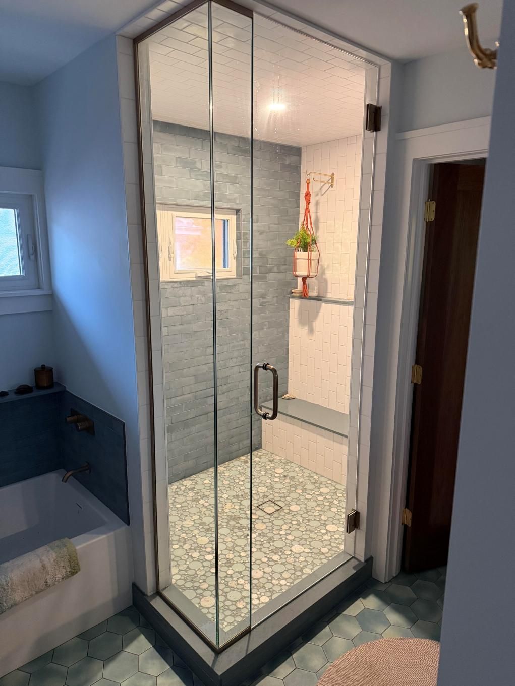 Glass shower stall with tiled floor and walls in a bathroom, beside a bathtub.