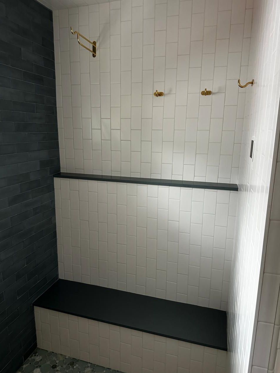 Small tiled shower or bath alcove with black bench, hooks, and a dark stone wall.