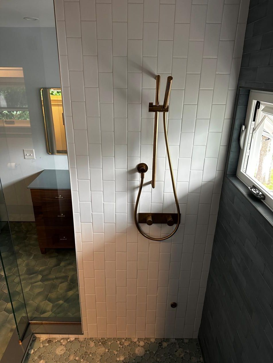 Bathroom shower with white tiled wall, handheld showerhead, and a dark hanging caddy.