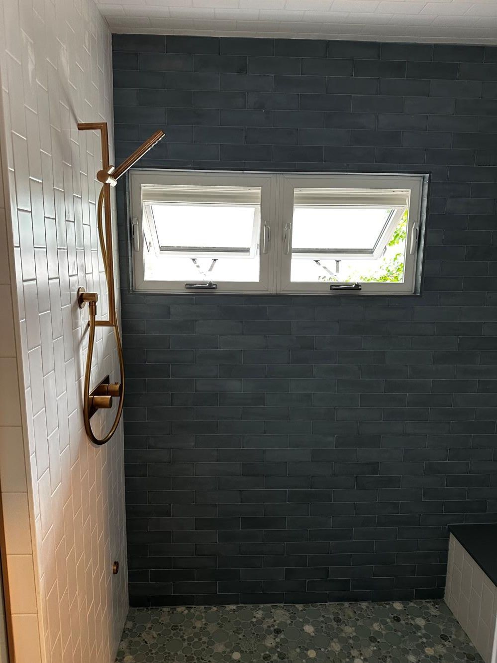 Small bathroom with dark tile wall, horizontal window, and shower fixtures on the left.