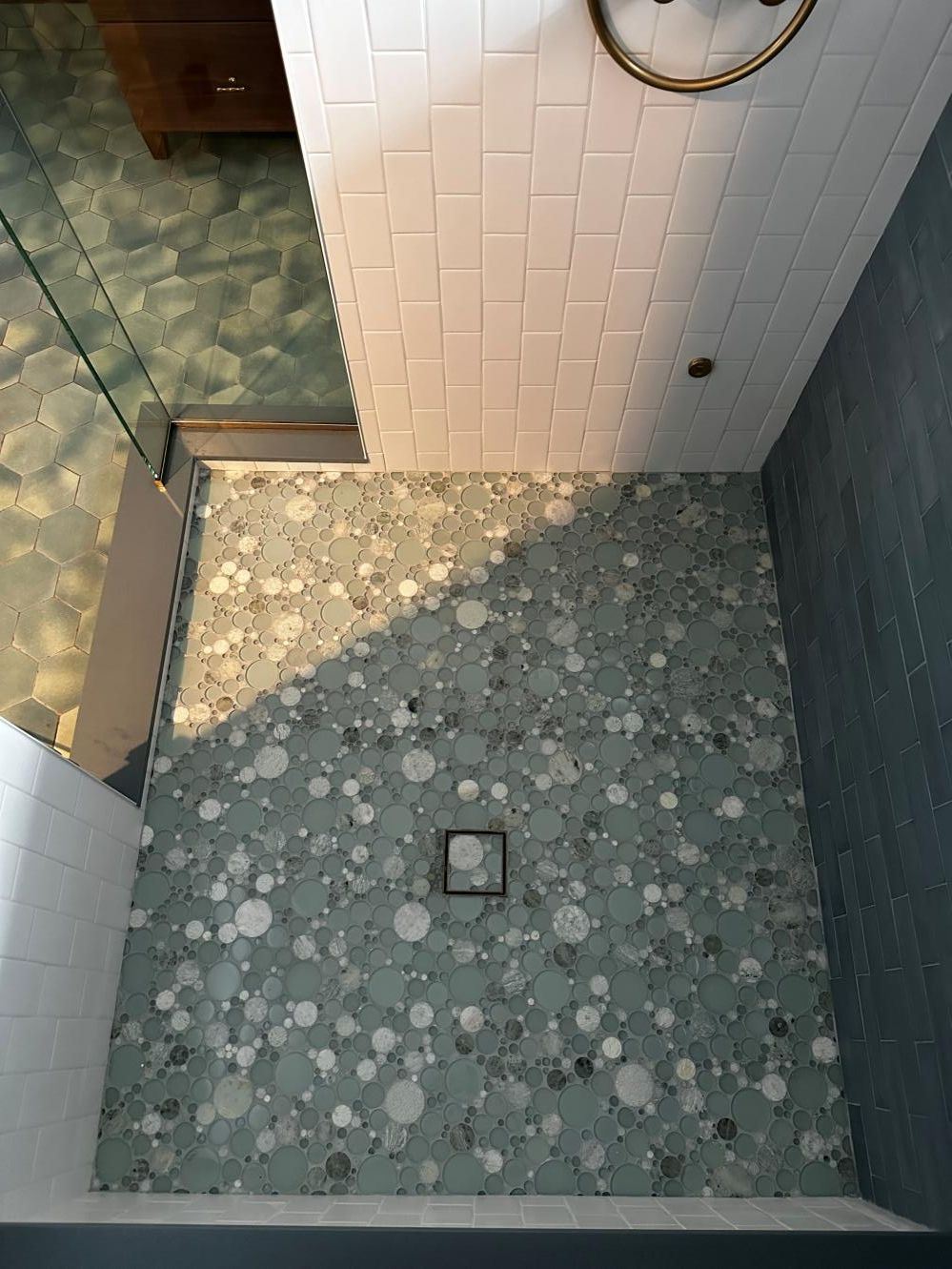 Small tiled shower stall with pebble floor, square drain, and partial glass door.