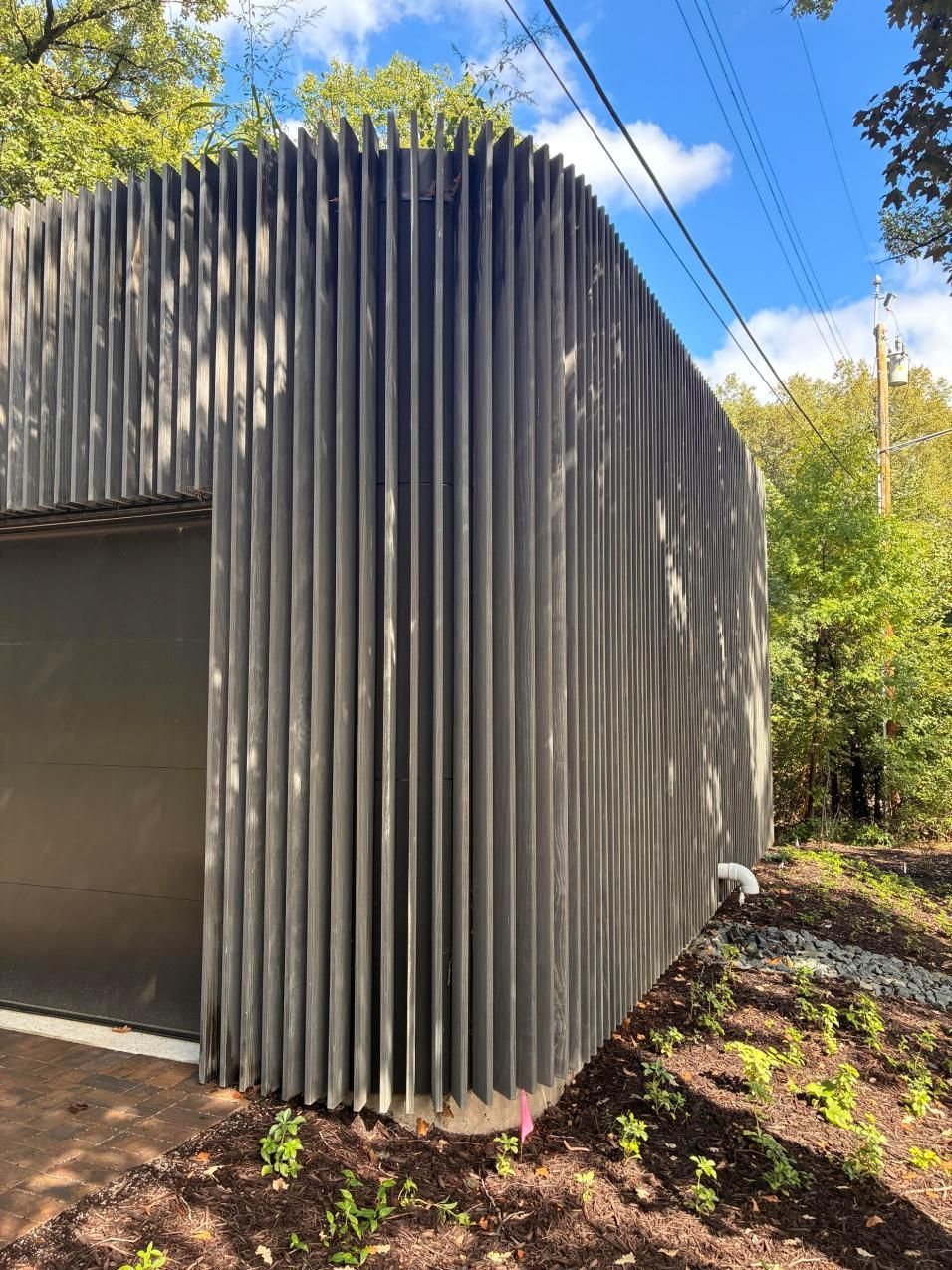 Modern building with a curved corrugated metal exterior beside trees under a blue sky