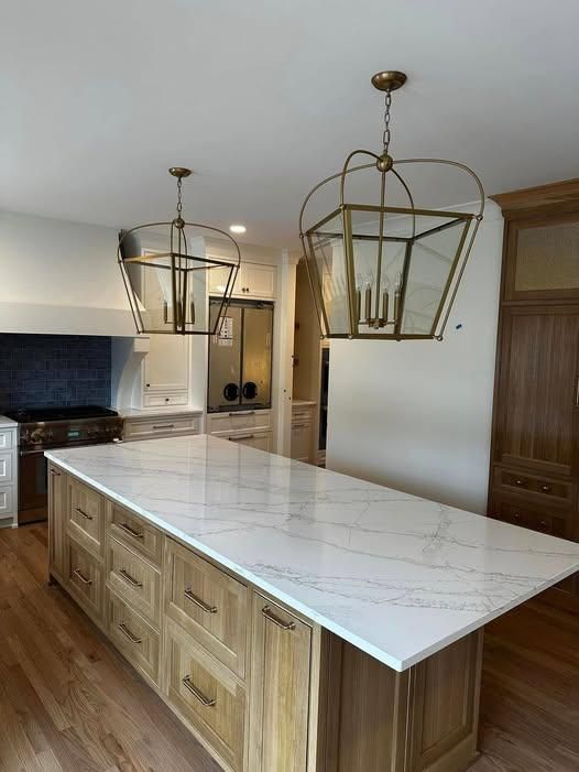 Modern kitchen with large white island, wood cabinetry, and two gold pendant lights