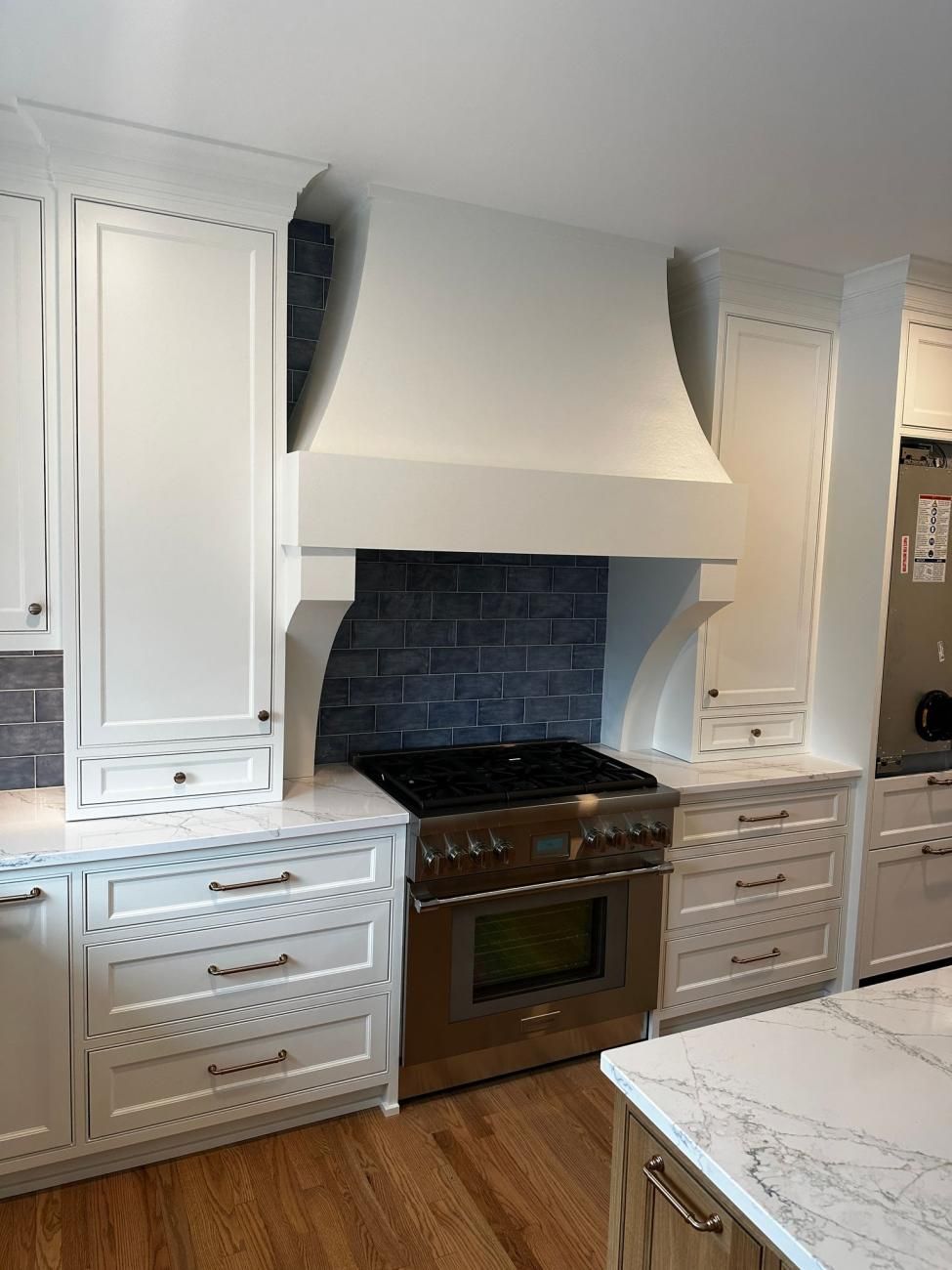 White kitchen with a stainless stove, tile backsplash, and built-in cabinets around a range hood.