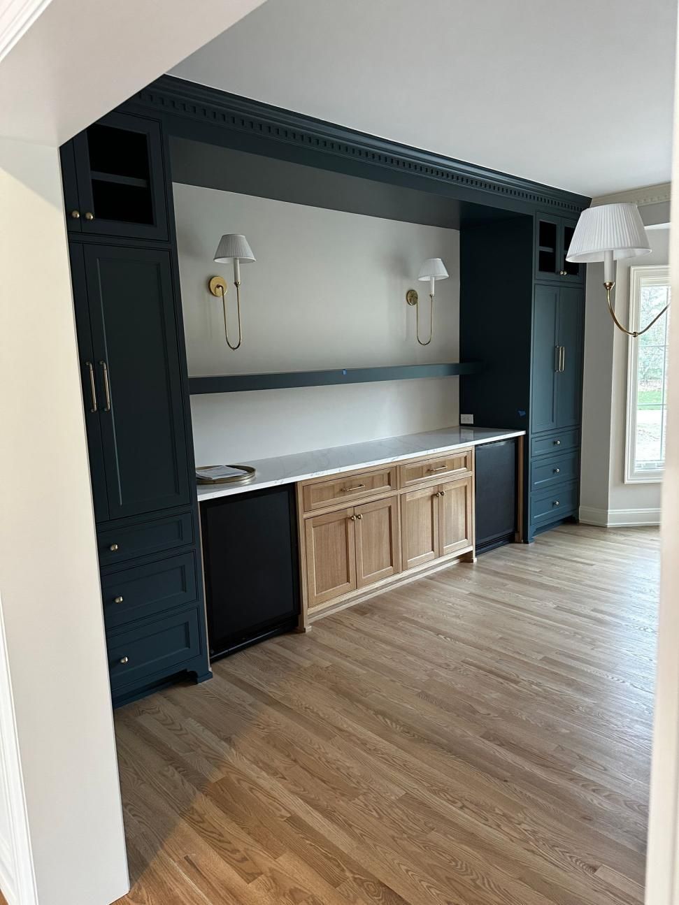 Modern room with built-in black shelving, wood cabinets, wall sconces, and light wood flooring
