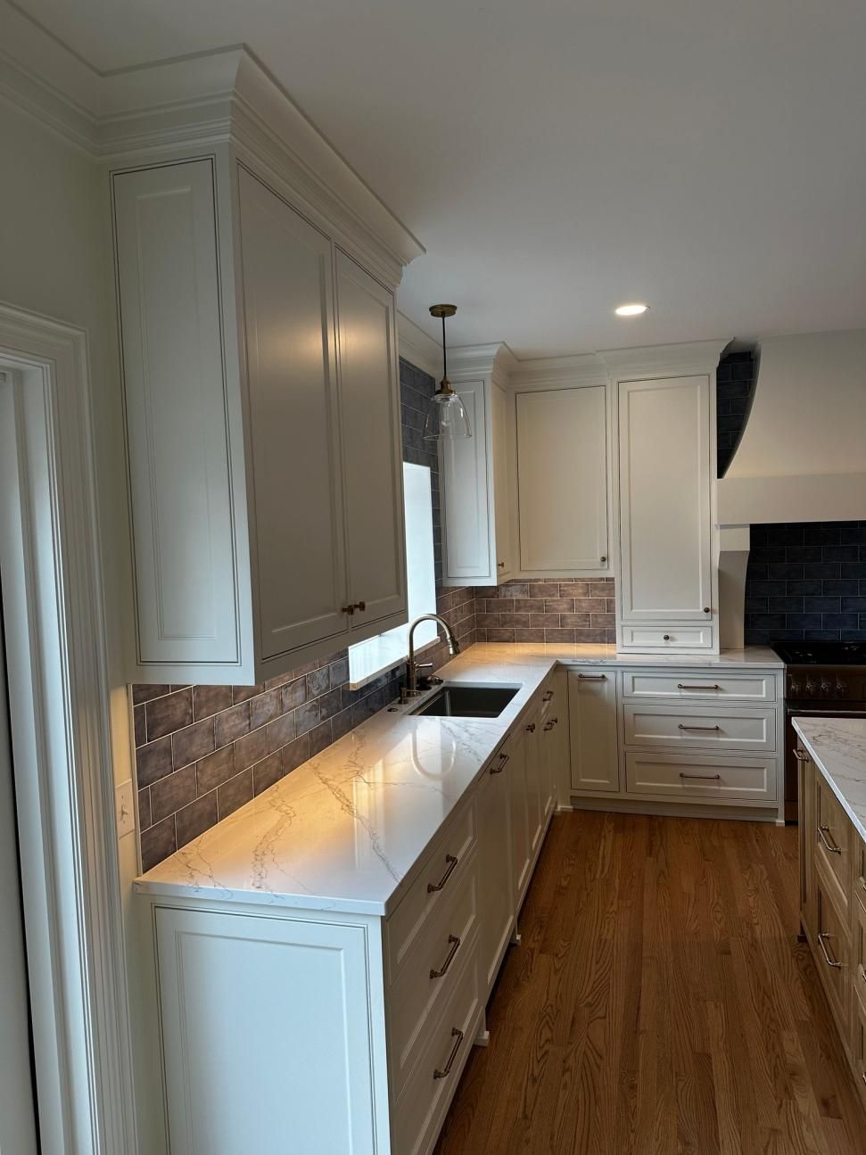Bright white galley kitchen with wood floors, marble countertops, and tile backsplash