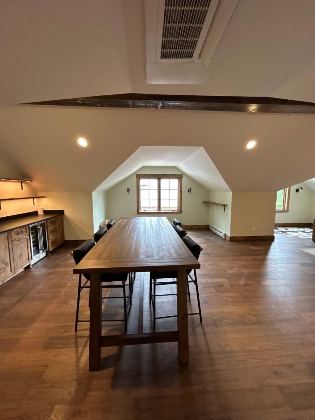 Spacious attic room with wood floors, a long table, and a windowed wall at the far end.