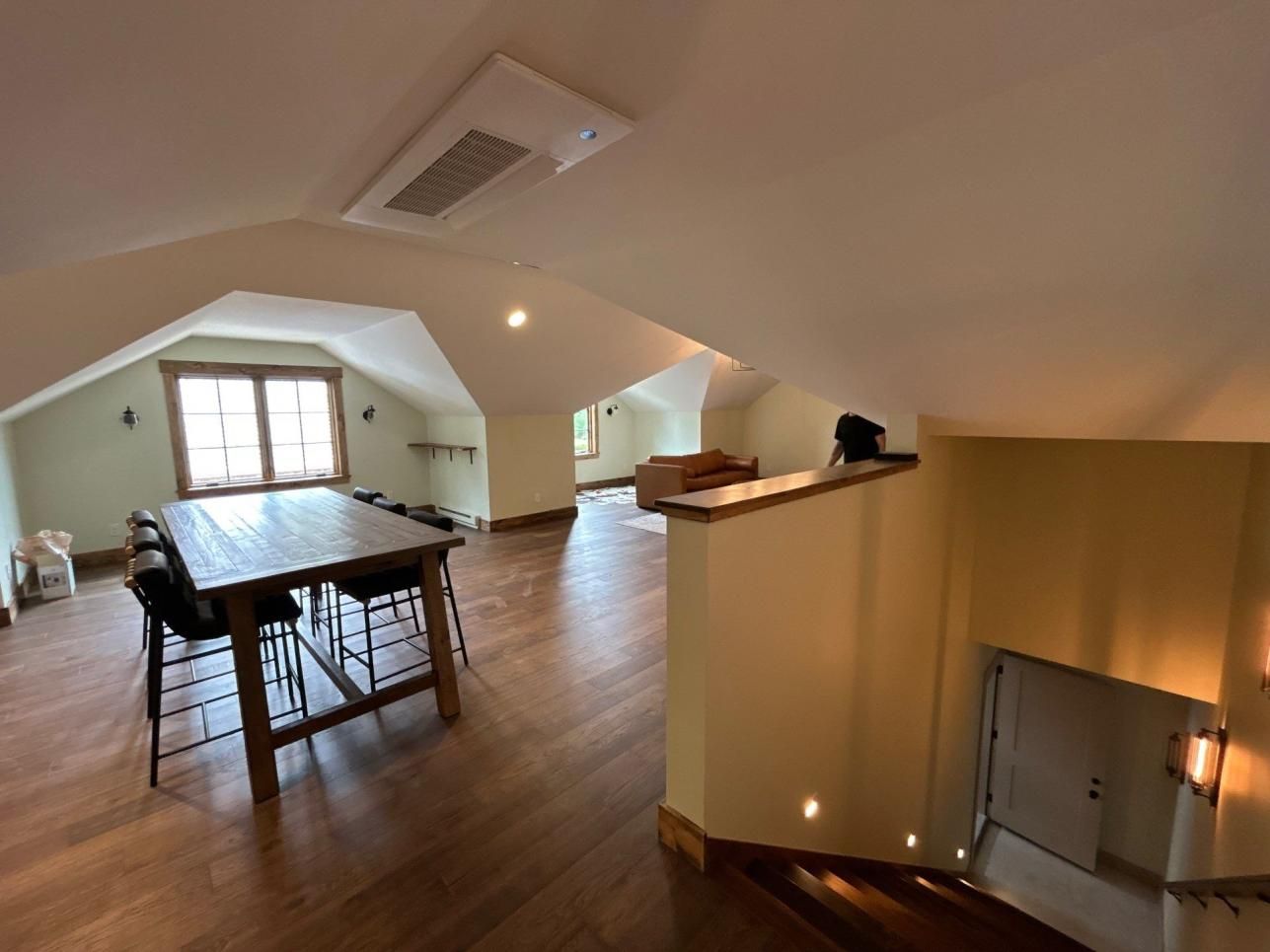 Open loft interior with wood floors, dining table, skylight, and stairway railing overlooking lower level