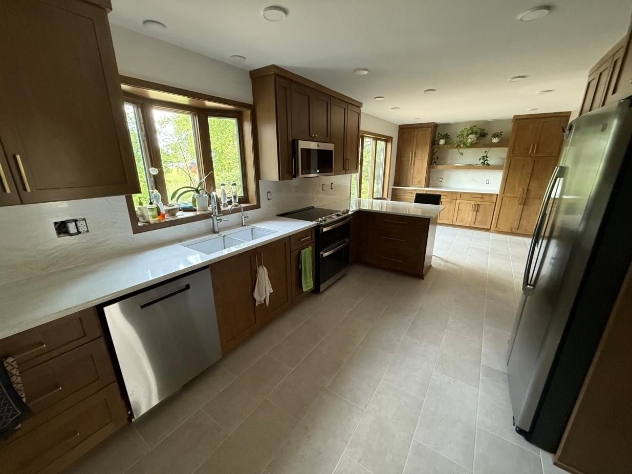Modern kitchen with dark wood cabinets, stainless appliances, tiled floor, and large windows.