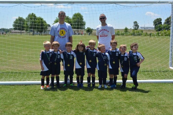 Youth soccer team posing with coaches in front of a goal on a sunny field