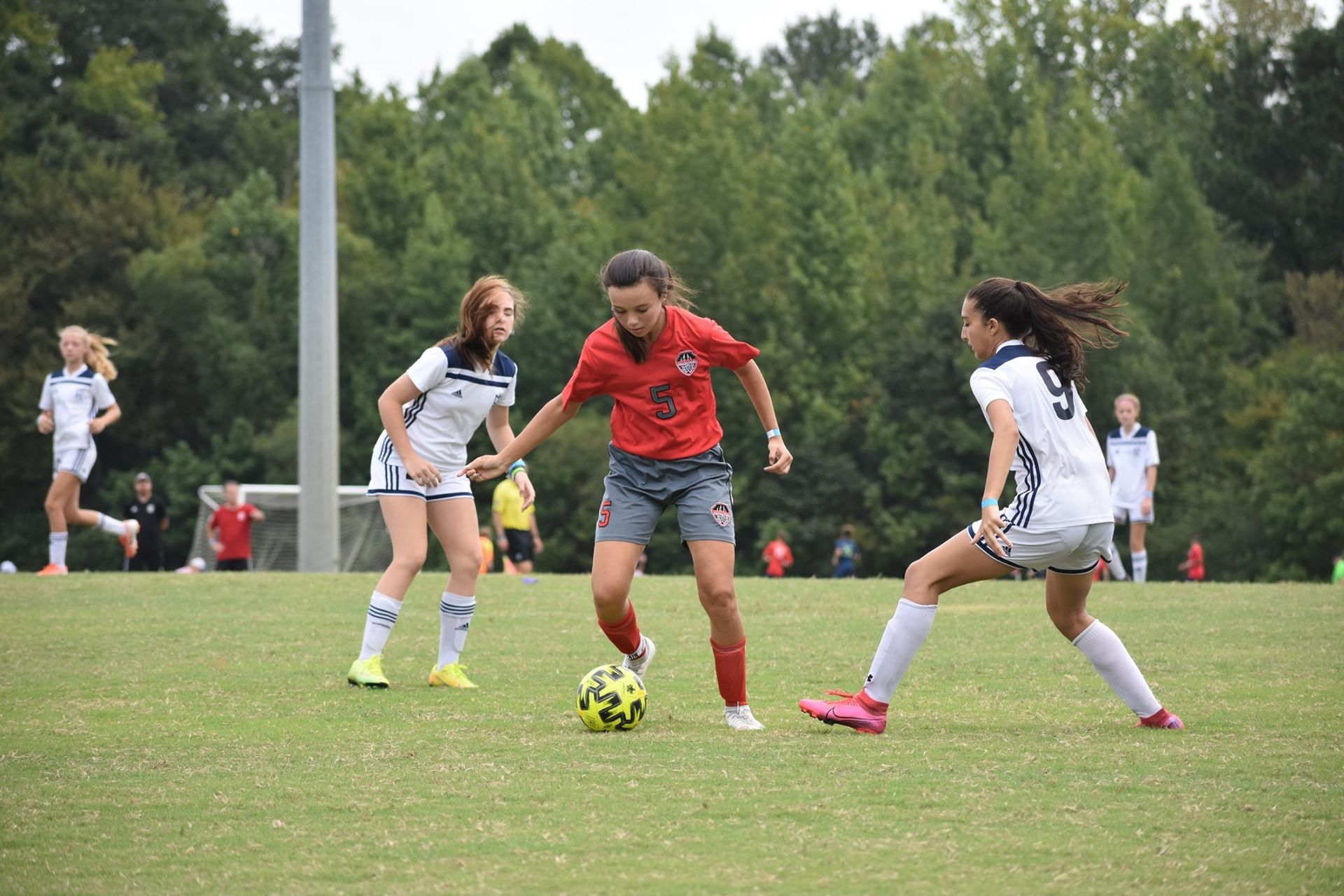 Soccer players in red and white uniforms compete for the ball on a grassy field.