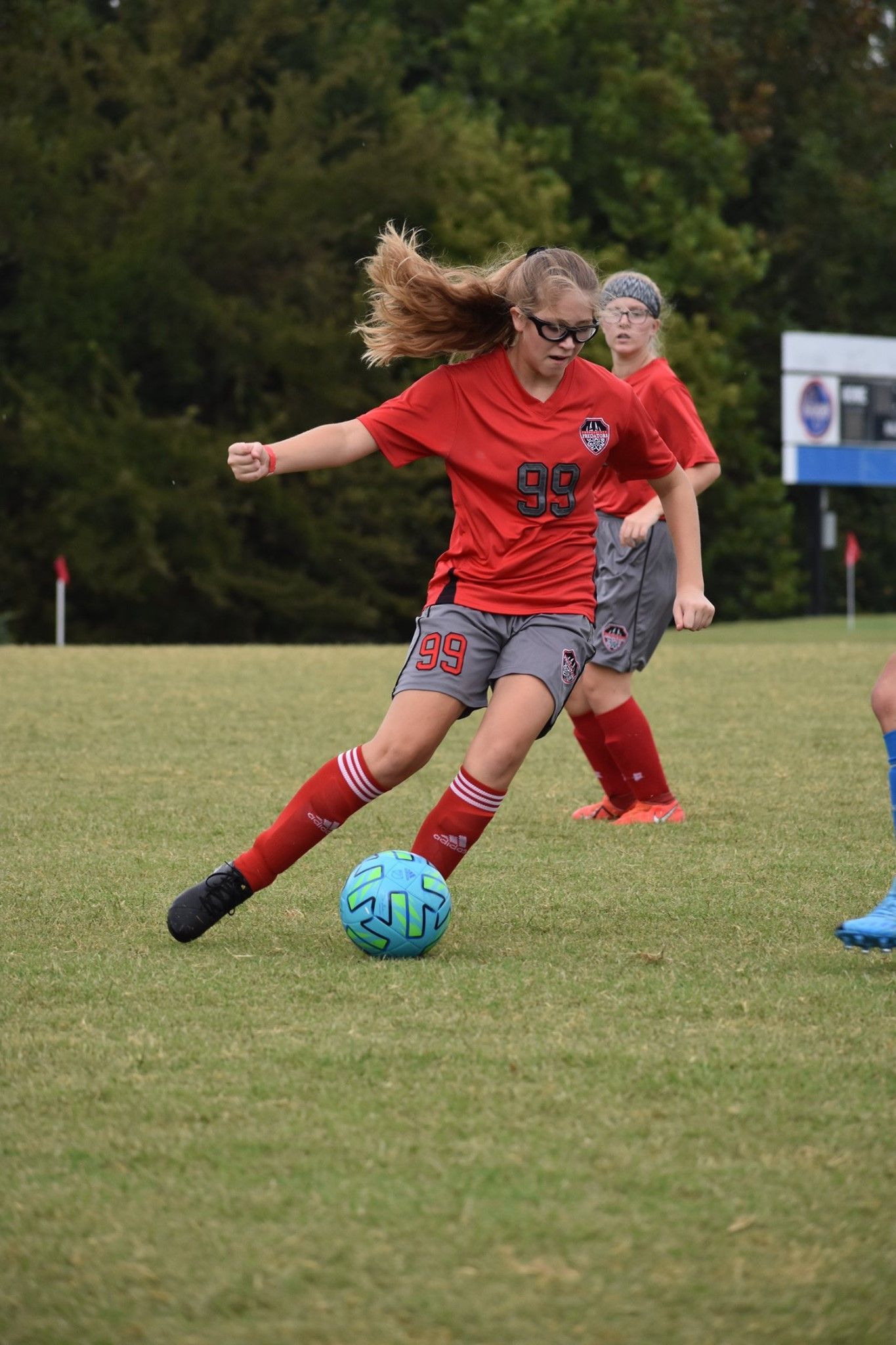 Soccer player in red dribbles a blue ball on a grassy field during a match