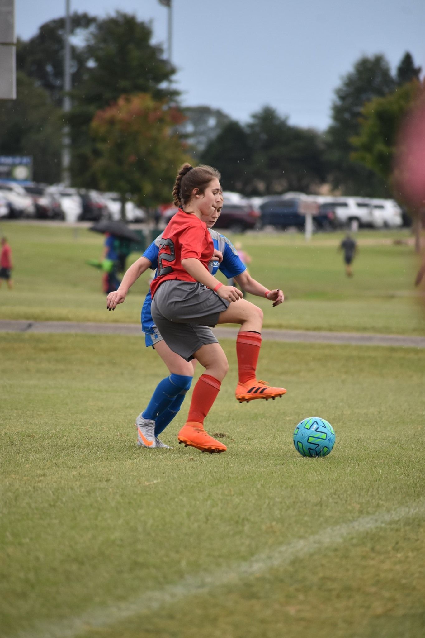Two soccer players in red and blue chase a blue ball on a grassy field