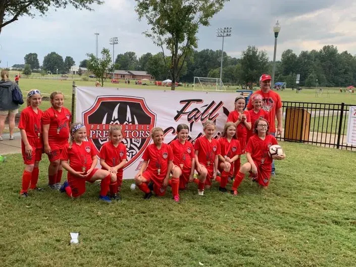 Group in red uniforms posing outdoors in front of a Fall Classic banner