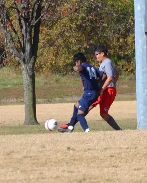 Two soccer players battling for the ball on a grassy field near a goalpost.