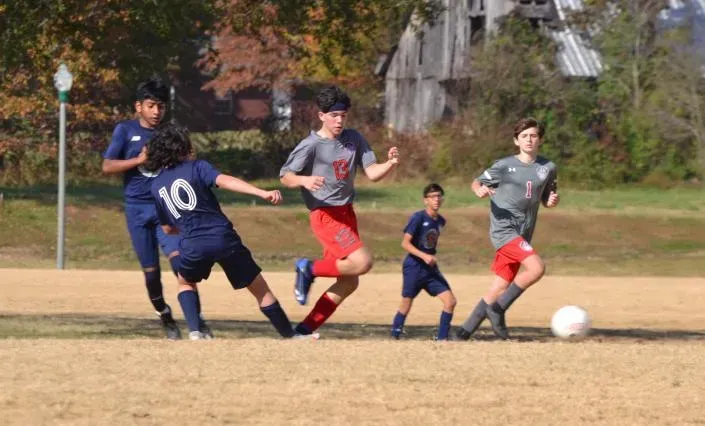 Youth soccer players chase a ball on a grassy field during a match.
