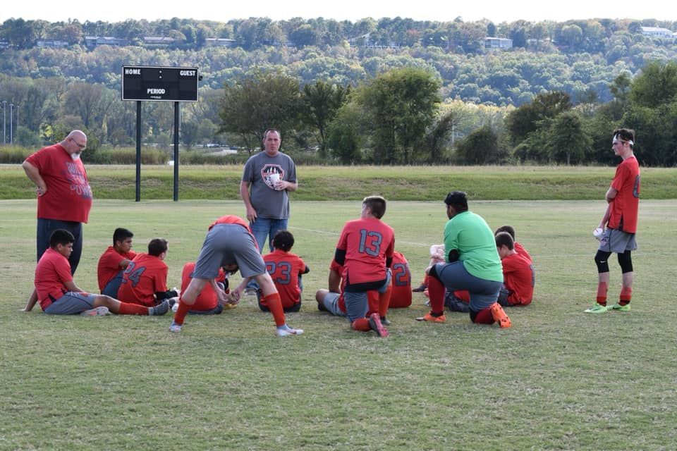 Soccer coach briefing players on a grassy field during practice
