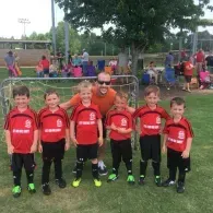 Youth soccer team in red jerseys posing with a coach on a grassy field