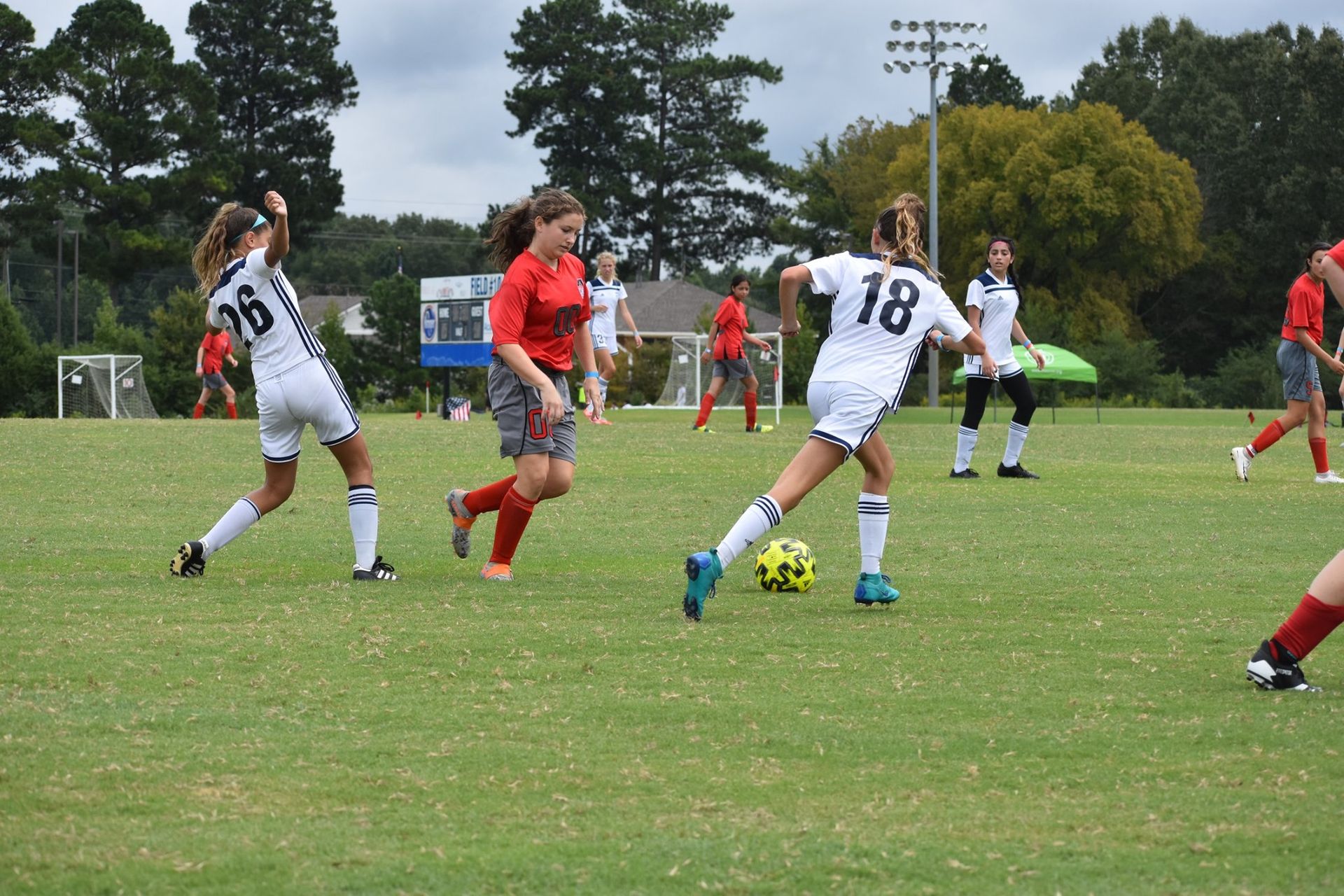 Soccer players in white and red jerseys compete for the ball on a grassy field.