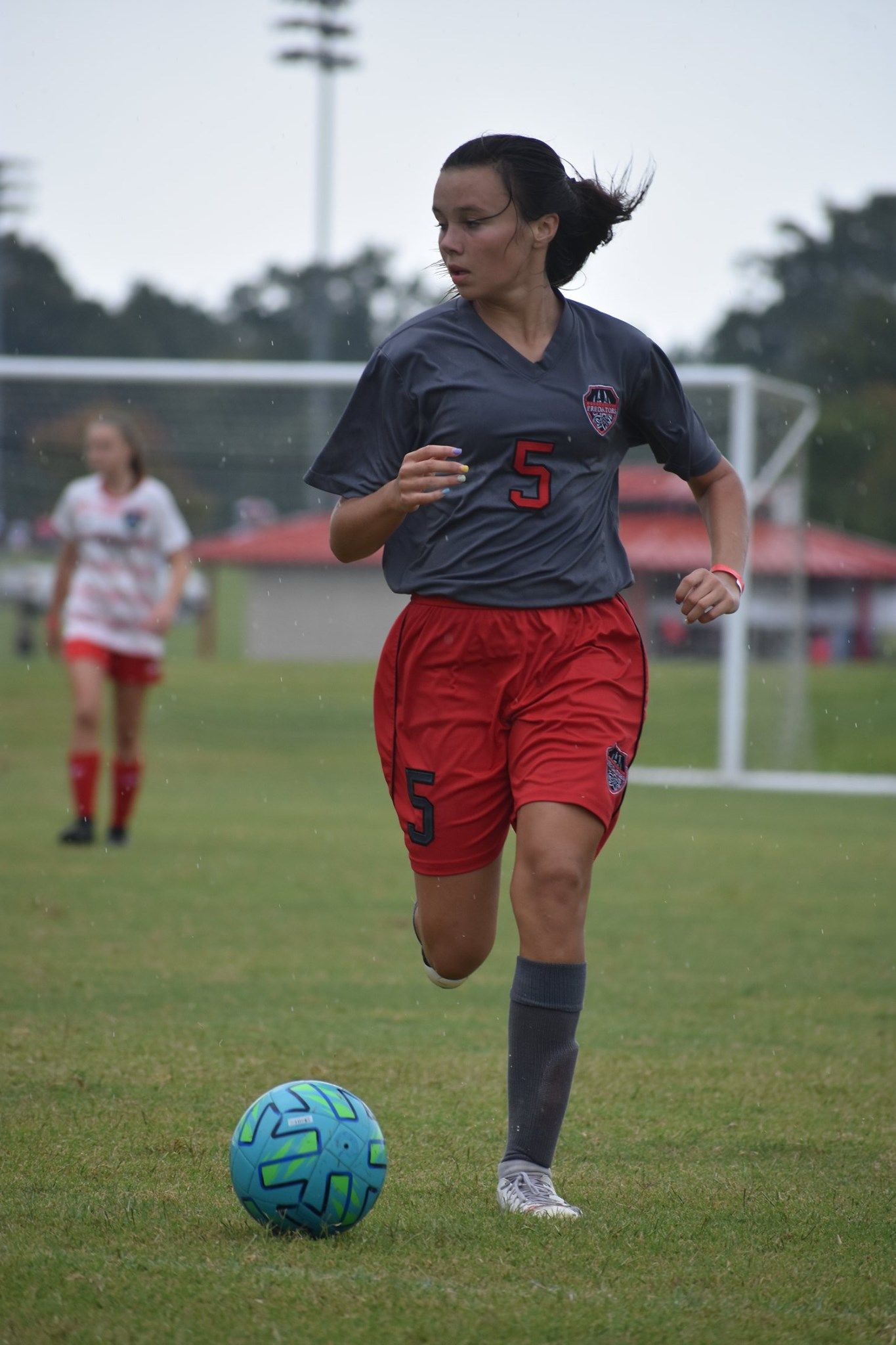 Soccer player in dark jersey and red shorts dribbles a blue ball on a field