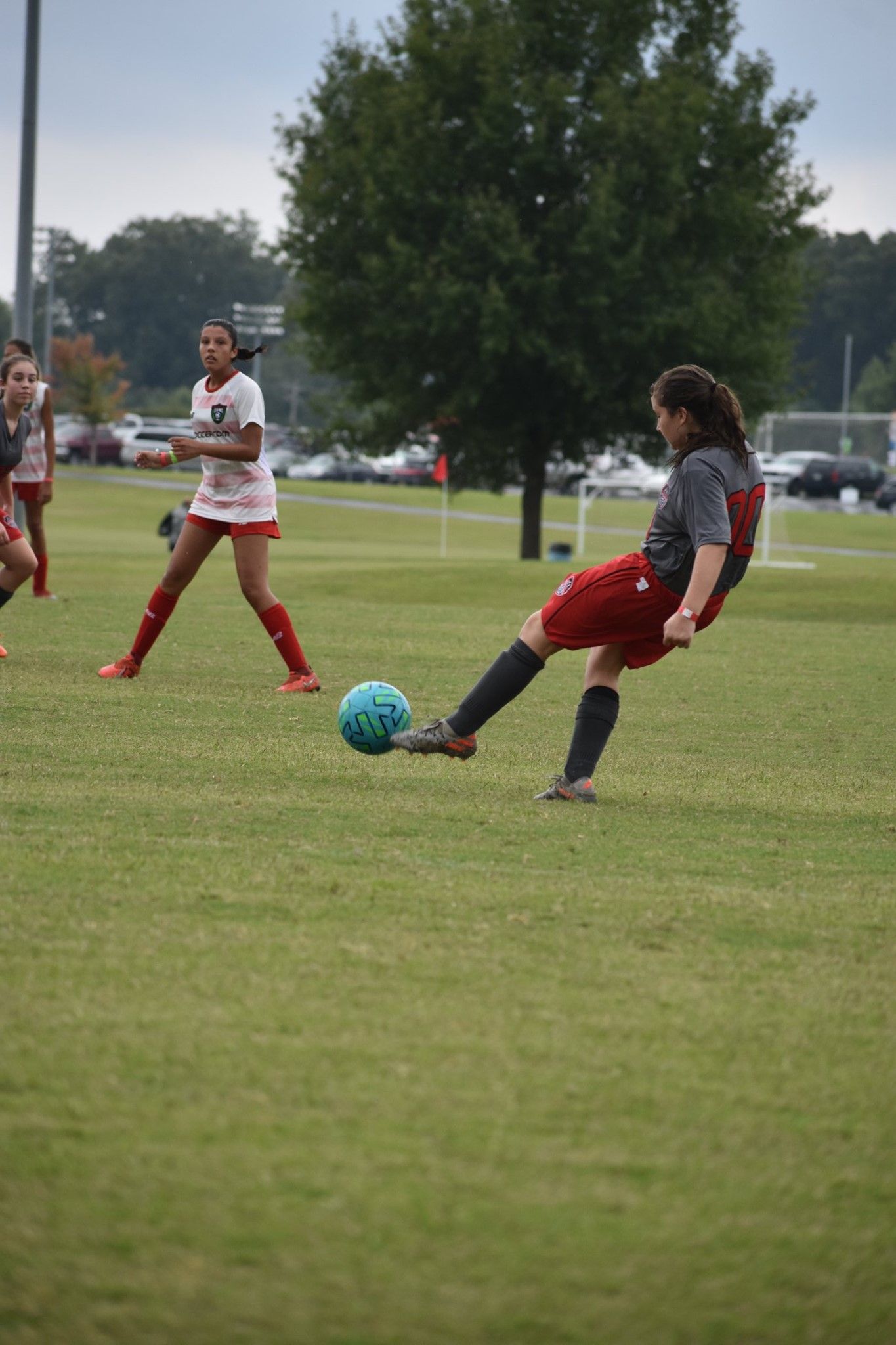 Soccer player in red and gray kicks a blue ball on a grassy field, with teammates in the background
