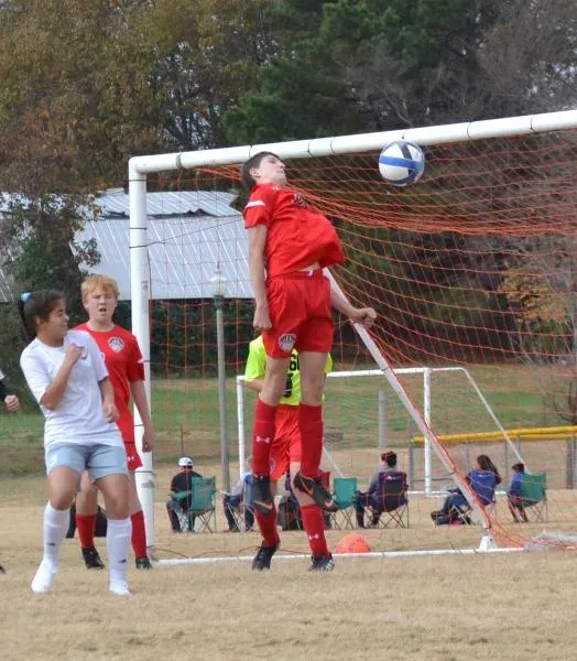 Soccer players leap for a header near the goal as the ball flies past the crossbar