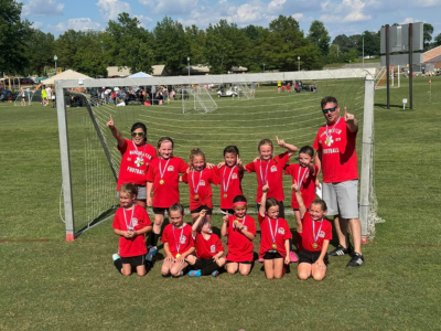Youth soccer team in red jerseys posing in front of a goal on a grassy field