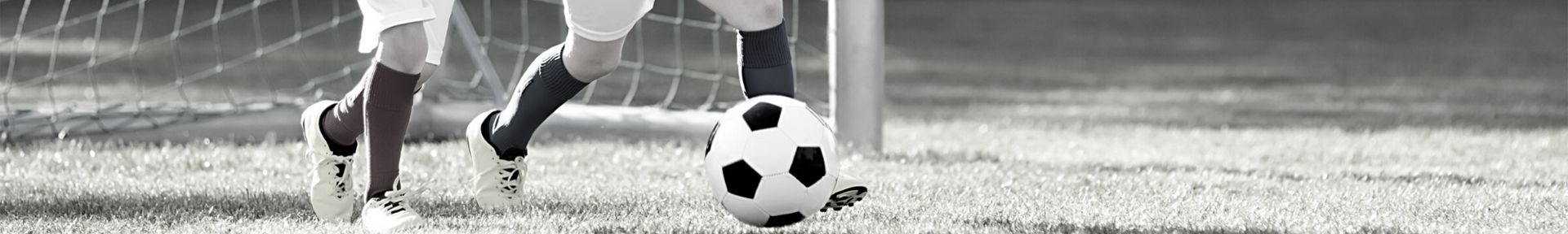 Soccer players’ legs near a ball on a grassy field during play