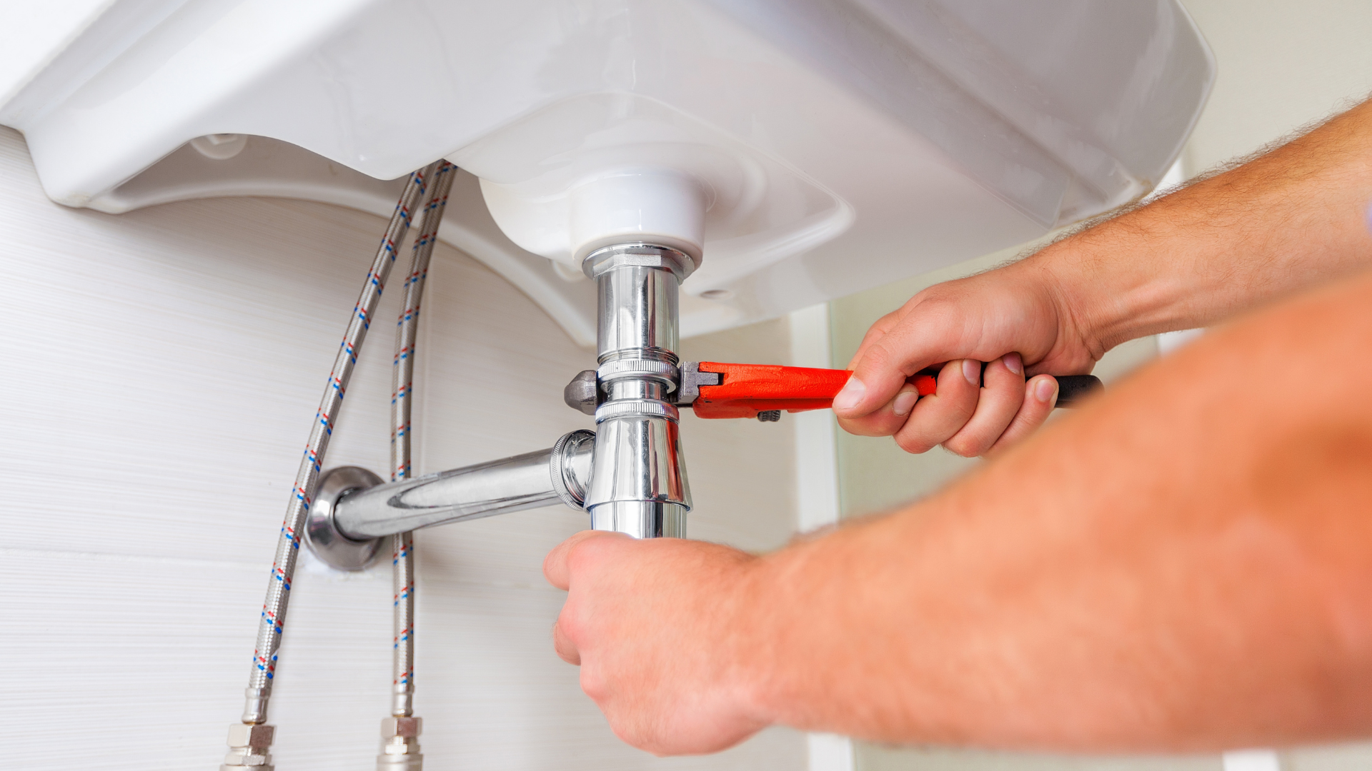 A person is repairing a sink pipe with a pair of pliers