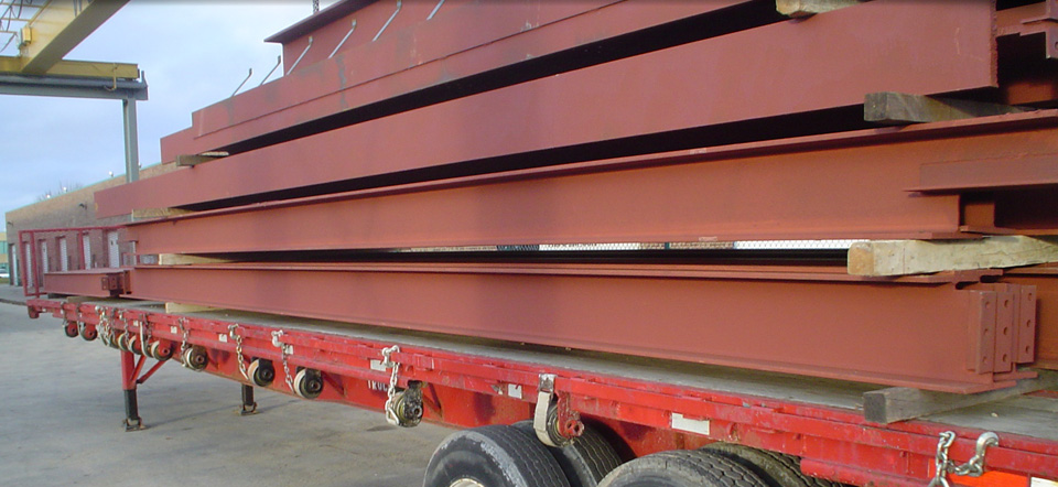 A red semi truck is carrying a stack of metal beams.