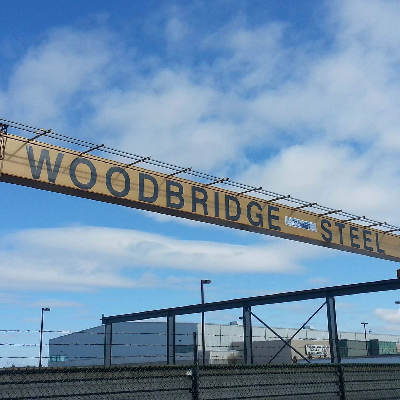 A woodbridge steel sign hangs over a fence