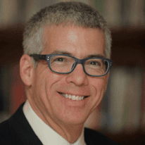 A man wearing glasses and a suit is smiling for the camera.