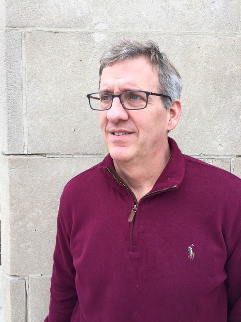 A man wearing glasses and a suit and tie is smiling for the camera.