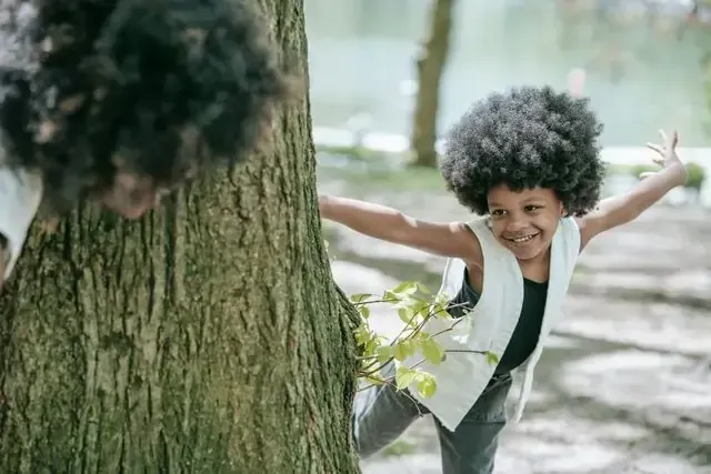 Smiling child with large afro and arms outstretched near a tree at a family assessment centre