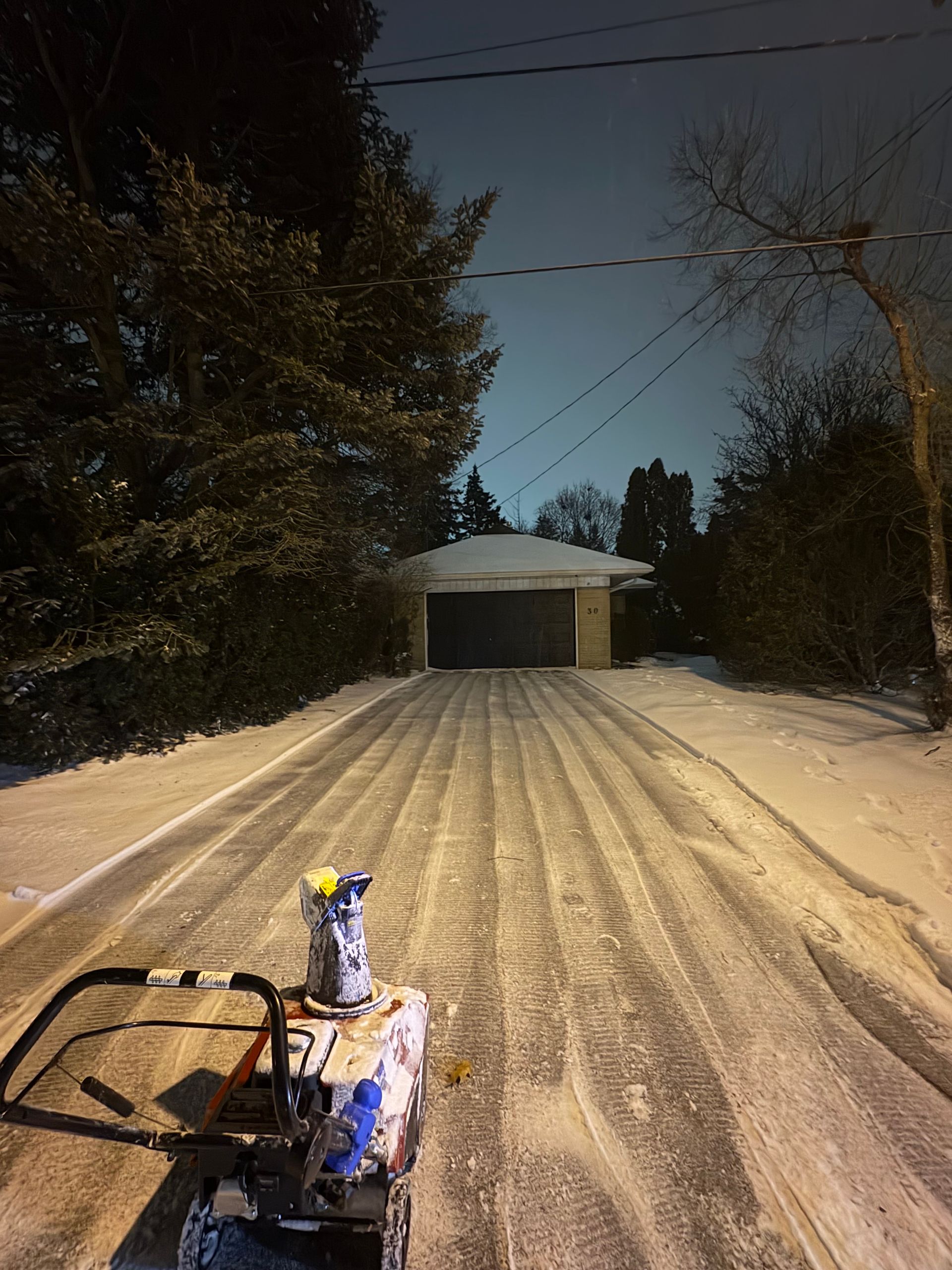 Snow-covered driveway leading to a garage, with a snowblower in the foreground.