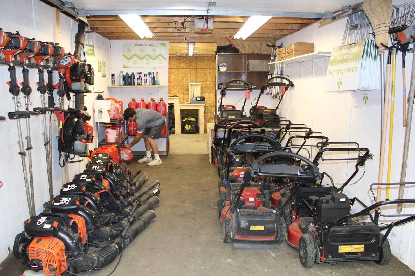 Garage filled with rows of lawn mowers and power equipment, with tools hanging on the walls