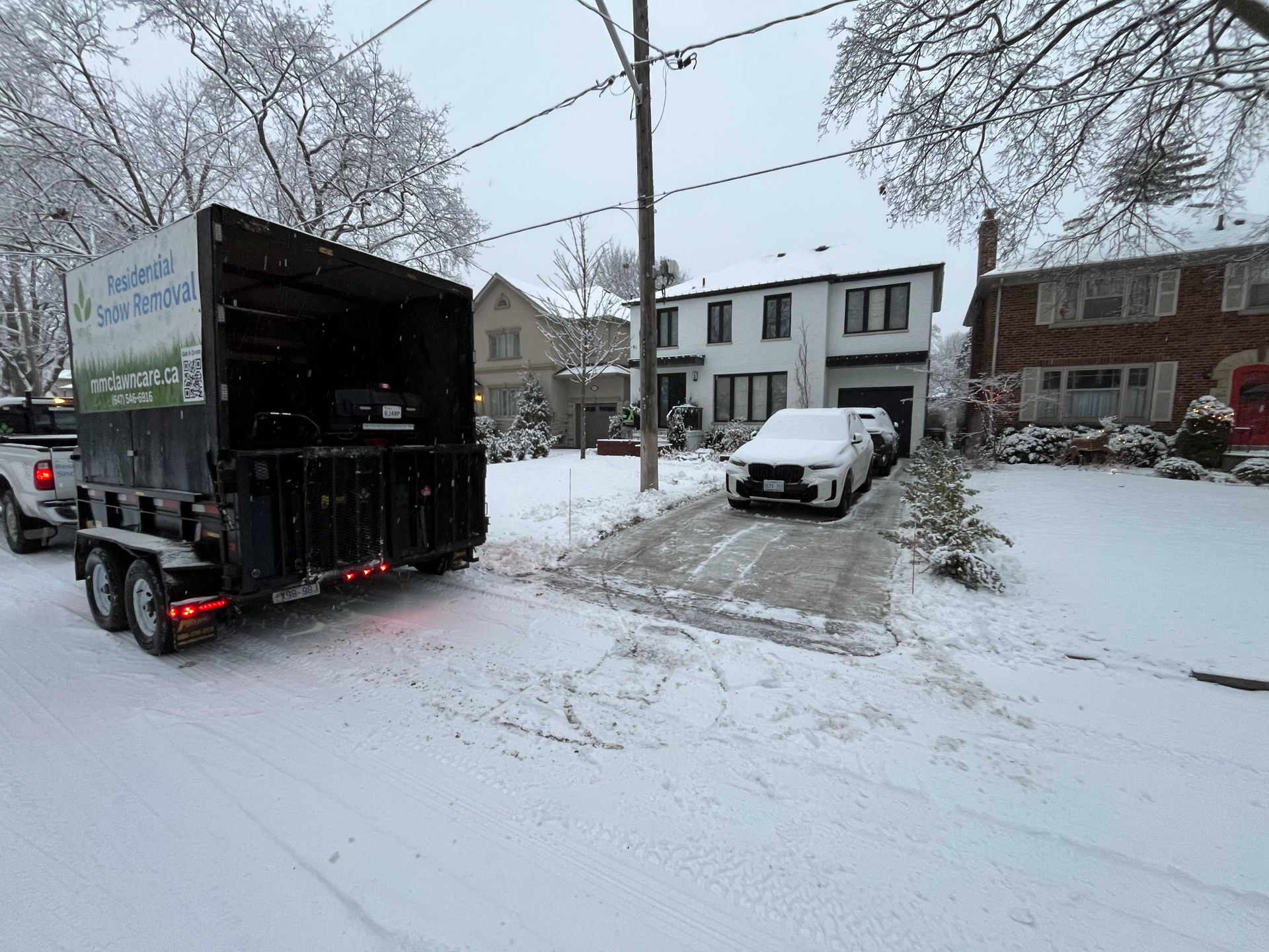 A trailer for yard waste removal parked in front of a white house on a snowy driveway.