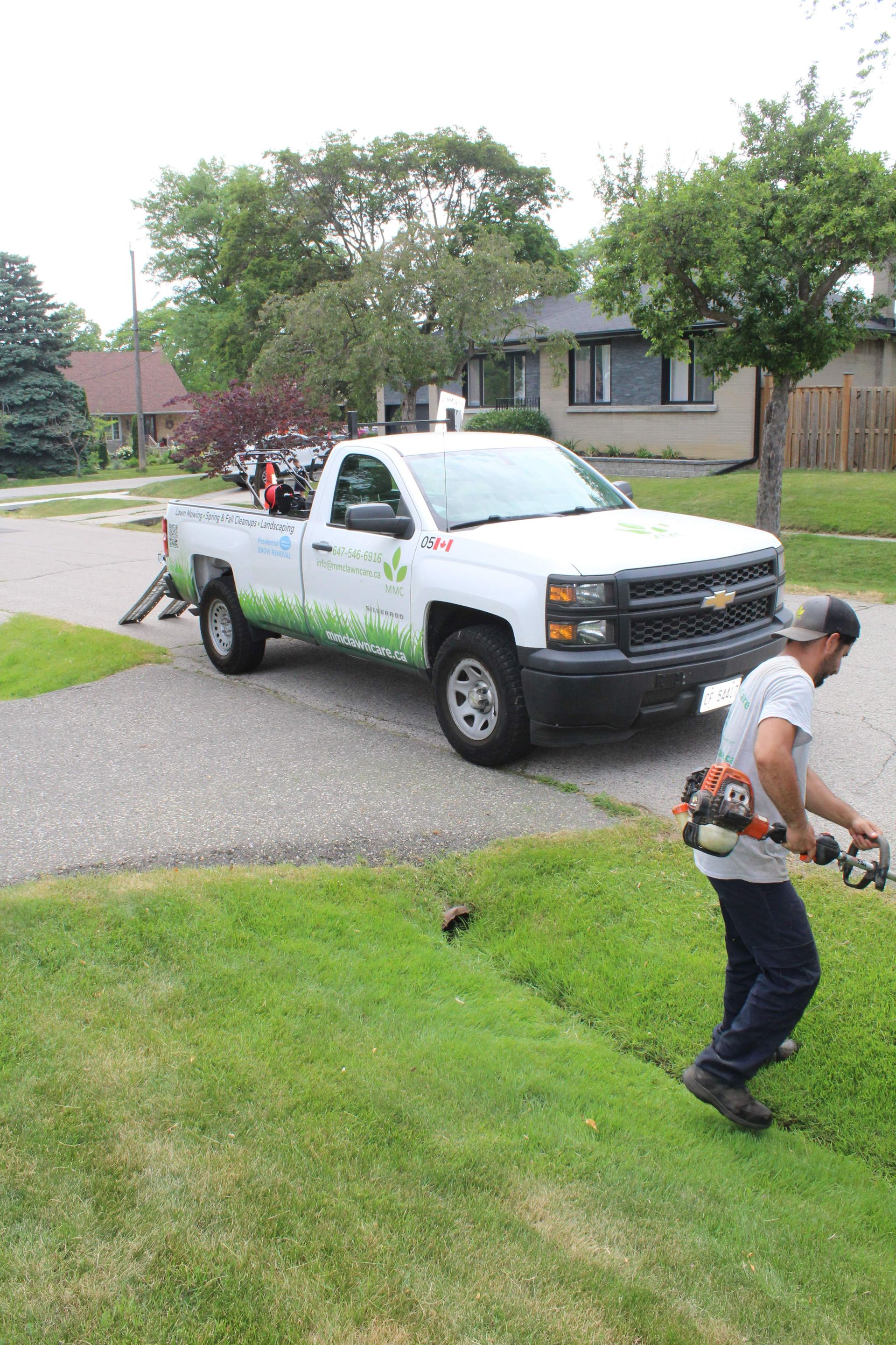 White pickup truck parked on a suburban street while a person walks across a lawn with tools in hand