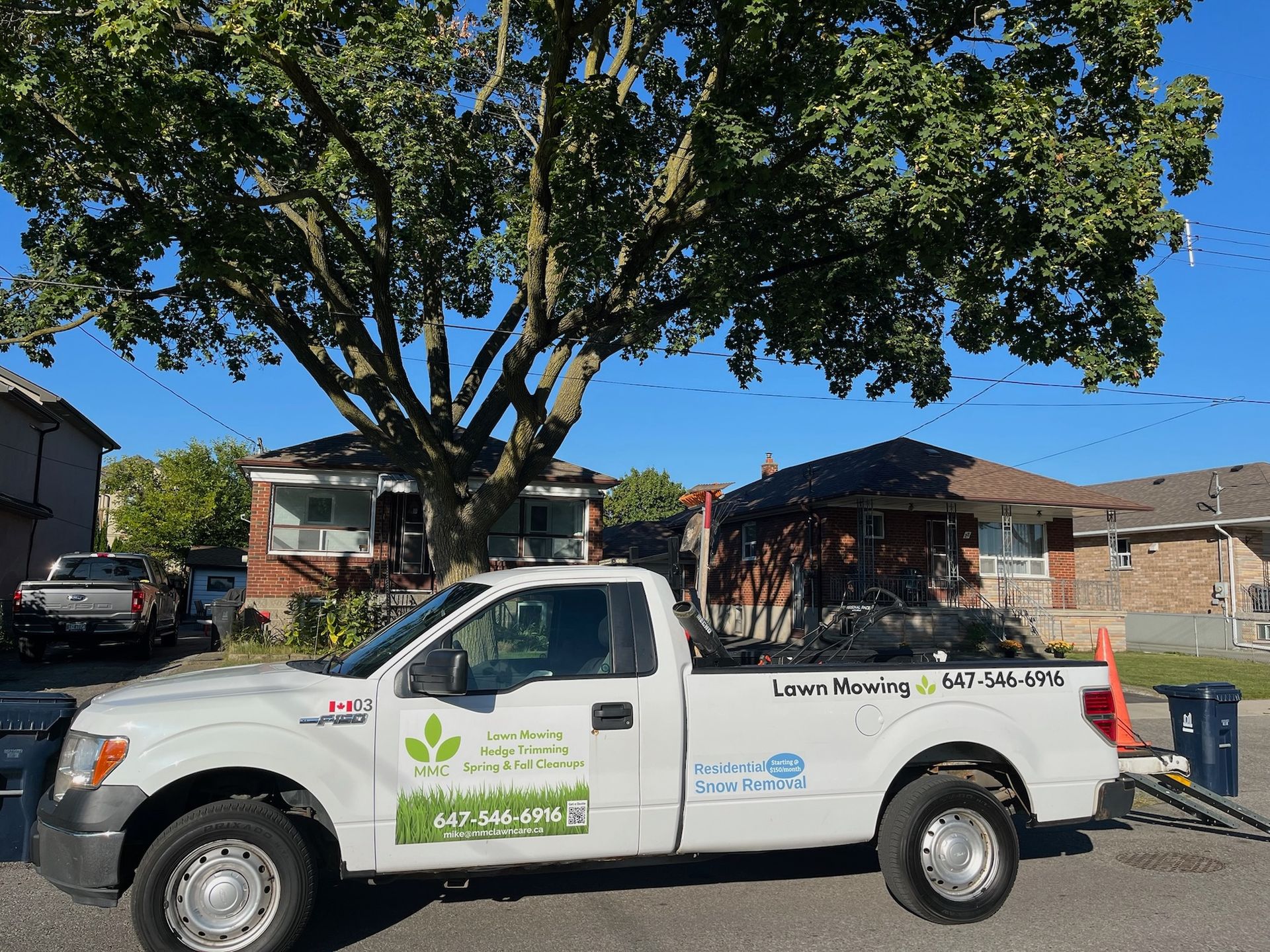 White pickup truck with business logos parked in front of houses; tree overhead.