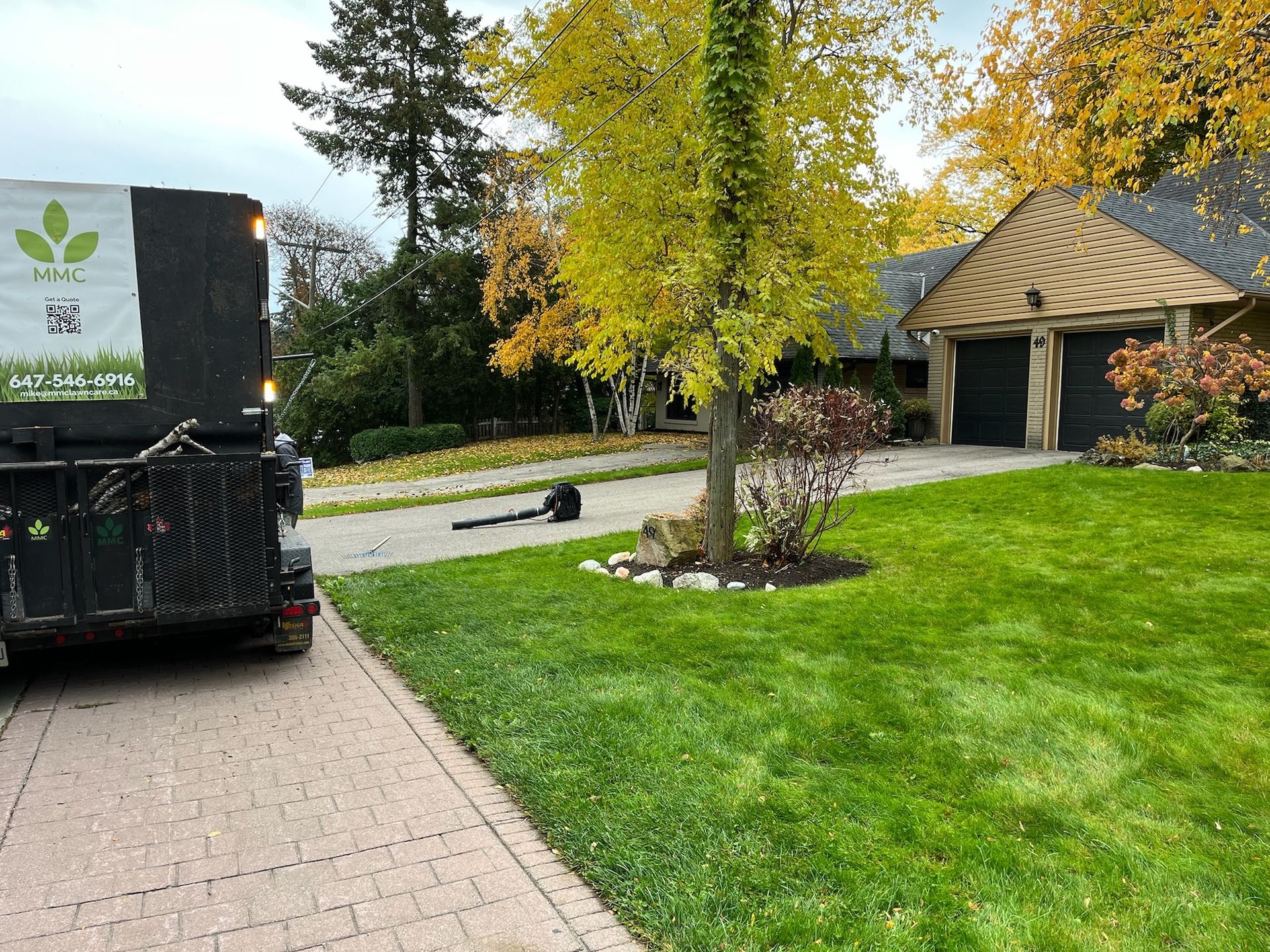 Landscaping truck parked on a driveway in front of a house, with fall foliage and green lawn.